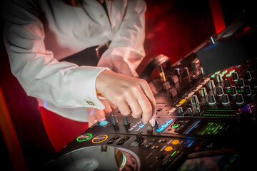 Close up DJ plays live set and mixing music on turntable console in the night club. Disc Jokey Hands on a sound mixer station at club party. DJ mixer controller panel for playing music and partying.