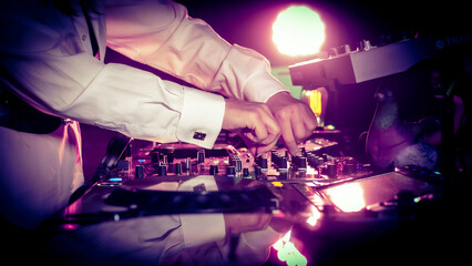 Close up DJ plays live set and mixing music on turntable console in the night club. Disc Jokey Hands on a sound mixer station at club party. DJ mixer controller panel for playing music and partying.