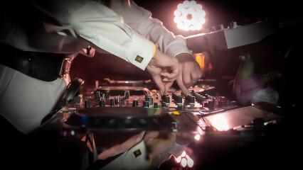 Close up DJ plays live set and mixing music on turntable console in the night club. Disc Jokey Hands on a sound mixer station at club party. DJ mixer controller panel for playing music and partying.