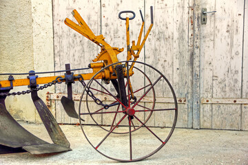 A vintage farm mechanized plow with a long pole for a hitch against the background of an old wooden gate.