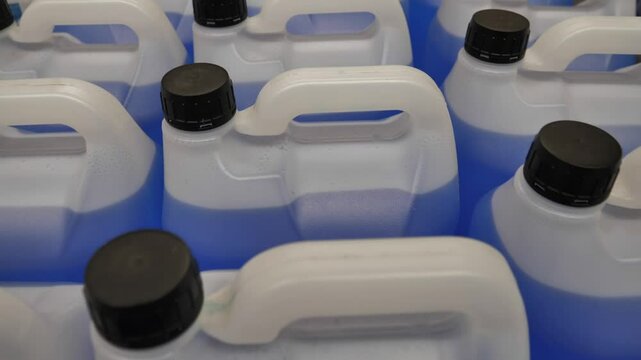 Rows of white  containers filled with a blue liquid are organised neatly in a warehouse ready for distribution.movement straight ahead, into the depth of the frame. view from above.