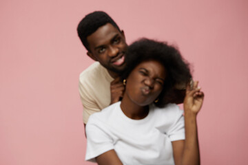 Fototapeta premium Young African couple enjoying a playful moment against a soft pink background, showcasing vibrant emotions and diverse styles, perfect for joyful lifestyle themes