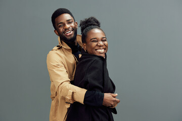 Happy African couple smiling together, enjoying a joyful moment in stylish outfits against a neutral gray background, showcasing love and connection