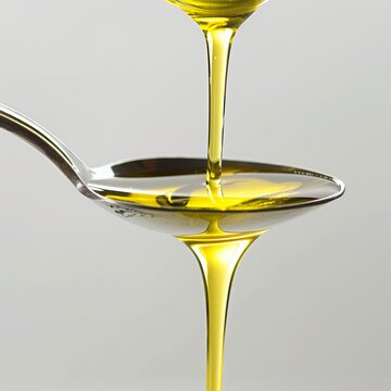 Olive oil pouring over the edges of a spoon on a white background.