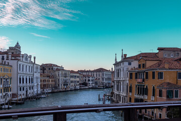 A stunning view of the Grand Canal in Venice, Italy, from a wooden bridge, capturing the city’s historic architecture and serene waterways under a bright blue sky. A perfect scene for themes of travel