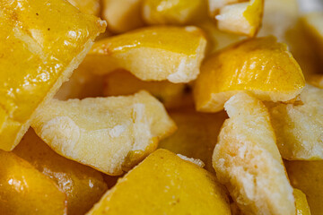 A close-up view of vibrant golden-yellow freeze-dried quince pieces against a white background. The texture and detail of the dried fruit are highlighted.