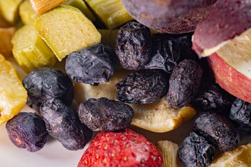 A colorful assortment of freeze-dried apples, bananas, strawberries, and blueberries displayed on a white surface. The vibrant textures and natural colors emphasize their preserved freshness.