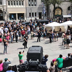 A bustling city square hosts an outdoor festival filled with people of all ages. Families watch performers while children engage with colorful activities, creating a vibrant atmosphere