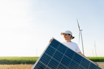 Woman wearing white cap and t-shirt with solar panel. Wind turbines in the background.