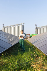 Female farmer with digital tablet on a modern farm using solar panels. Agricultural silos in the...