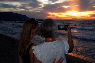 Mother and daughter take photos of the sunset on a mobile phone