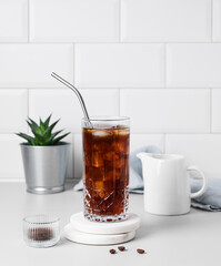 Cold brew coffee in a glass with ice and straw on a light table against a white brick background