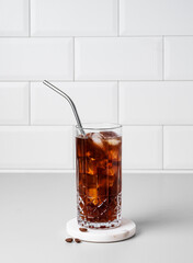 Cold brew coffee in a glass with ice and straw on a light table against a white brick background