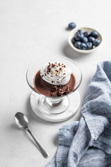Chocolate pudding in a glass with whipped cream on a light background