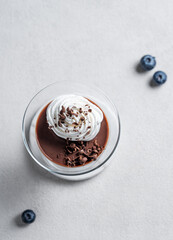 Chocolate pudding in a glass with whipped cream on a light background with berries.