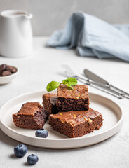 Chocolate brownie with nuts cut into pieces on a plate with blueberry and mint  on a light background