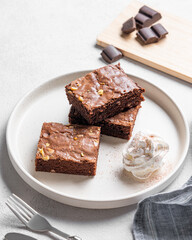 Chocolate brownie with nuts cut into pieces on a plate with whipped cream on a light background