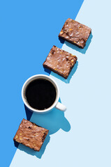 Pieces of chocolate brownie and a cup of espresso coffee on a blue background with hard light.