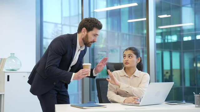 Businessman sexually harasses a young female coworker places hand on shoulder at workplace in business office. Adult male employee flirts with a shocked worried woman colleague, expression of concern