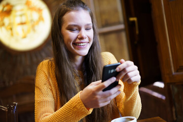 Cheerful Young Woman Relaxing and Enjoying a Tasty Coffee while Texting on Her Smartphone