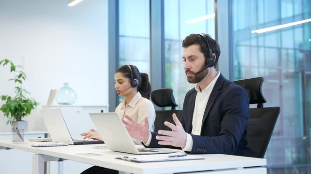 Corporate operators working with headsets in customer support service on helpline telesale using laptop. A team of call center agents, men and women helping online, speak on a video call in the office