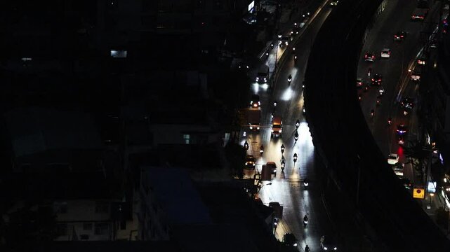 Aerial view footage of a dimly light urban street at night. Bangkok traffic road in night time showing less vehicles on colorful light vibe cities top view. Night cityscape road traffic aerial view.