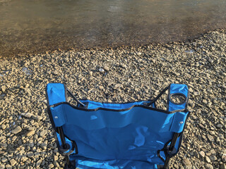 Relaxing by the river with a blue camping chair on a gravel shore during a sunny afternoon