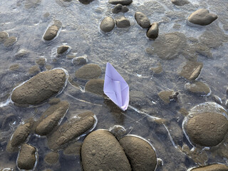 Paper boat rests on smooth stones by the water's edge during a calm afternoon