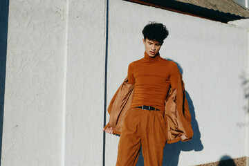 Stylish young man in an orange outfit posing against a white wall