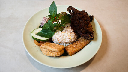 Traditional Indonesian Kecombrang Rice with Fried Spiced Duck Tempeh Tofu Assorted Sambals Fresh Basil and Cucumber Served on a Light Green Plate on Neutral Table Background