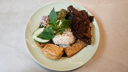 Traditional Indonesian Kecombrang Rice with Fried Spiced Duck Tempeh Tofu Assorted Sambals Fresh Basil and Cucumber Served on a Light Green Plate on Neutral Table Background