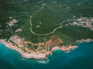 A stunning aerial view of a coastal cliff with turquoise waters, winding roads, and lush greenery....