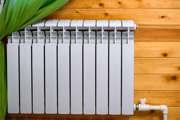 Aluminum heating radiator on a wooden wall. Heating of the room with steam heating of a wooden house.