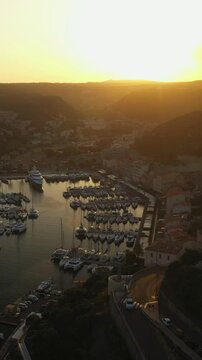Vertical video of a sunset in an ancient town with old houses around the yacht marina. City harbor with anchored yachts and sailboats aerial video at sundown time  
