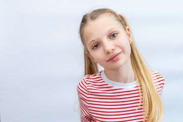 Fototapeta premium Smiling blonde girl in striped shirt. Portrait of a cheerful blonde girl with ponytails and blue eyes, wearing a red and white striped shirt against a plain background. Space for text.