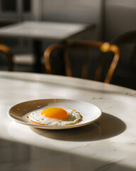 Sunny side up fried egg on a white plate in a bright cafe setting during morning hours