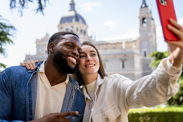 Obraz premium Cheerful multiethnic tourists taking a selfie with smartphone in front of a cathedral in a city, enjoying vacation