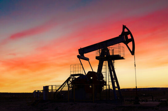 Crude oil pump jack at oilfield on atmospheric sunset backround. Fossil crude output and fuels oil production. Oil drill rig and drilling derrick. Global crude oil Prices, energy, petroleum demand