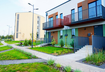 Obraz premium Modern townhouses in a residential area. New apartment buildings with green outdoor facilities in sustainable enviroment. Street with Two-story townhouses. Townhouse along sidewalk with green lawn.