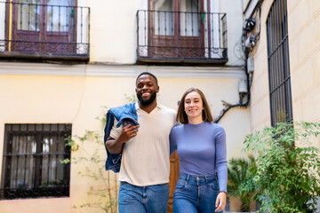 Smiling young couple stepping into the city energy as they leave their apartment. Concept of positivity and diversity.