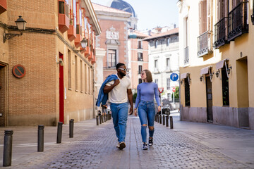 Multiethnic couple enjoying a walk down a cobblestone street in a city during a sunny day