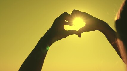 silhouette of the heart in the rays of the sun. make heart symbol with hands. valentine. love sign. freedom of travel. happiness of a woman's dream. heart against the sky. declaration love to person