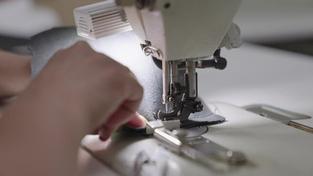 needle with thread sewing machine works workshop. Sewing tailor products from high-quality leather fabric. seamstress sews sewing machine workshop. hands close up. woman seamstress works business
