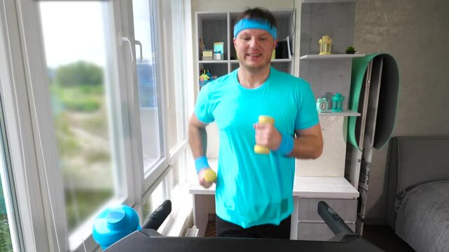 Cardio training on a treadmill with 1 kg dumbbells in your hands. A young man runs on a treadmill at home. Slow motion. Weight loss concept.