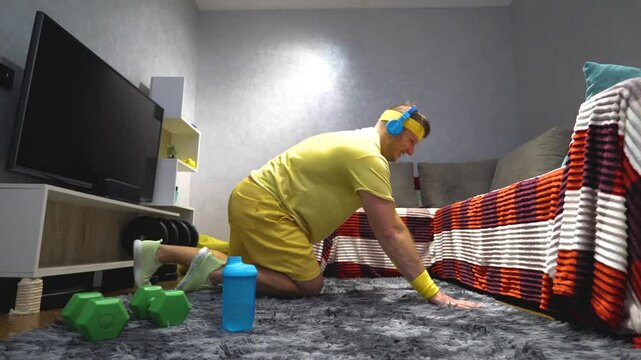Comic funny athlete at home doing push-ups on the floor while listening to music on headphones. A young funny guy training at home. Workout in the interior. Slow motion.