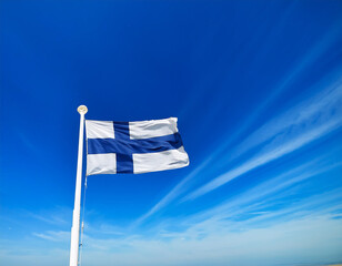 Fototapeta premium Simple Finnish flag, white with a blue cross, waving elegantly in a soft blue sky.