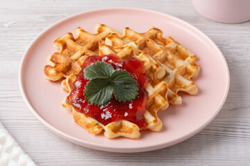 Delicious waffles topped with strawberry on a pink plate with a light wooden background