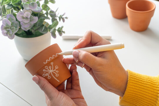 Decorating a small terracotta pot with a white marker by the hands of an adult woman