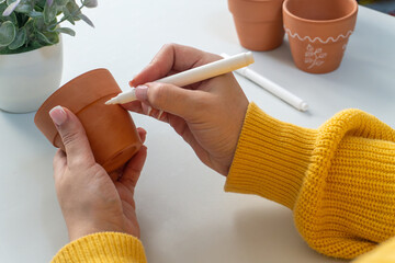 Close-up of womans hands in a cozy yellow sweater painting on a clay pot