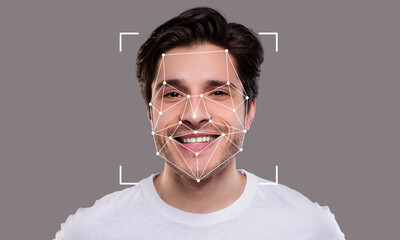 A young man is smiling while being analyzed by facial recognition technology. The geometric overlay...